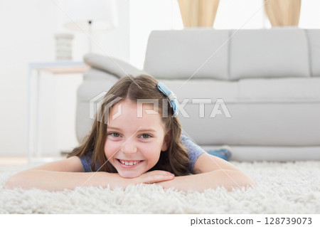 female child lying on stomach on white fluffy rug in living room with blue hair bow 128739073
