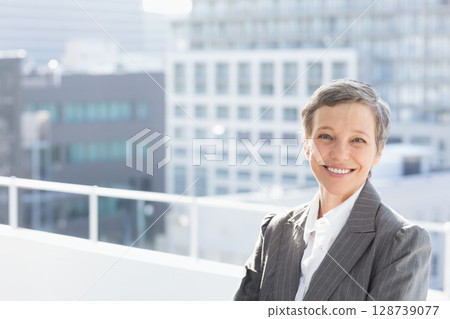 Woman leaning against white metal railing on rooftop deck overlooking office buildings, copy space 128739077