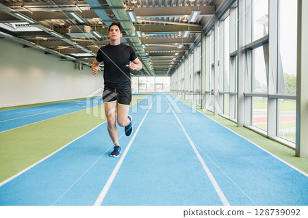 Young adult male athlete sprinting on synthetic track in training facility, with running shoes Young adult male athlete sprinting on synthetic track in training facility, with running shoes 128739092