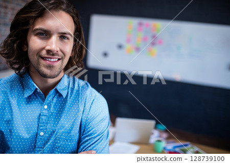 Young adult man standing at desk in office workspace, using laptop beside sticky notes, copy space 128739100