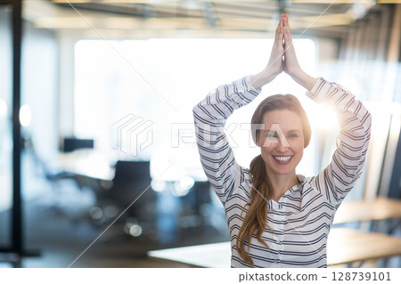 Business-casual woman stretching arms overhead in modern office with glass partitions, copy space Business-casual woman stretching arms overhead in modern office with glass partitions, copy space 128739101