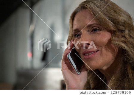 Woman holding smartphone while smiling during phone conversation in modern indoor lobby, copy space 128739109
