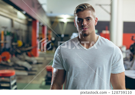 Athletic male standing in modern gym free weight area, with benches, dumbbell racks and squat rack 128739110