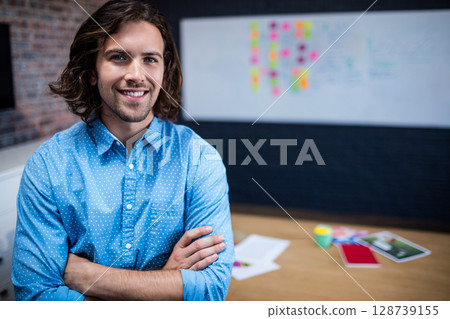Man standing crossing arms and smiling in modern office, with whiteboard and coffee cup Man standing crossing arms and smiling in modern office, with whiteboard and coffee cup 128739155