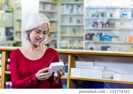 Senior woman examining medicine box inside pharmacy, with wooden counter and shelving 128739162