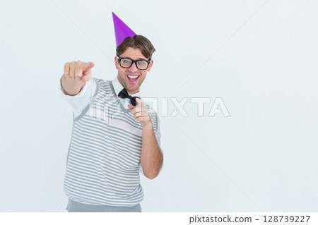 Young man pointing at camera in studio, with purple party hat and black glasses, copy space 128739227