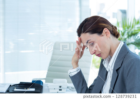 Mid adult businesswoman sitting at office desk, leaning head on hand with phone, papers, copy space 128739231