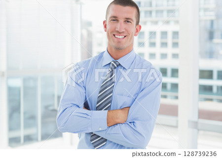 Man standing smiling crossing arms in office with dress shirt, striped necktie and windows 128739236