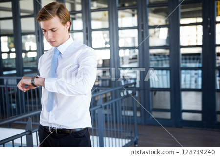 Businessman checking analog wristwatch in office lobby by glass walls, tracking time precisely 128739240