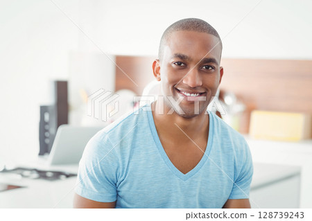 African American man sitting while smiling at countertop in home kitchen, using laptop and speaker 128739243
