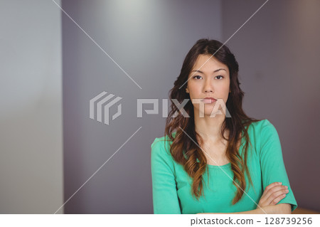 Female standing with arms crossed indoors against smooth grey panel walls, with neutral expression 128739256