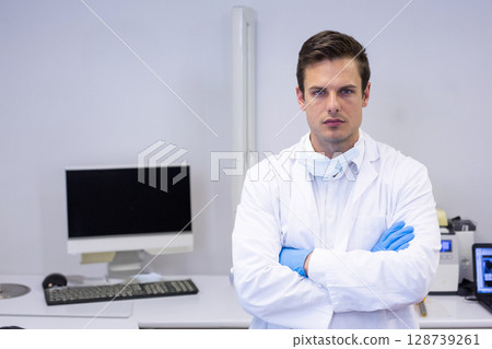 young man standing with arms crossed in lab office, with computer monitor and keyboard, copy space 128739261