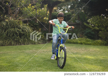 One young adult bi-racial man riding blue neon green BMX bicycle across backyard garden, smiling 128739269
