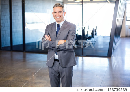 Senior man standing confidently in office lobby, with glass conference room and linear LED lights Senior man standing confidently in office lobby, with glass conference room and linear LED lights 128739289