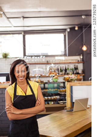 Woman standing behind wooden counter in modern cafe, showcasing pastries and laptop, copy space Woman standing behind wooden counter in modern cafe, showcasing pastries and laptop, copy space 128739298
