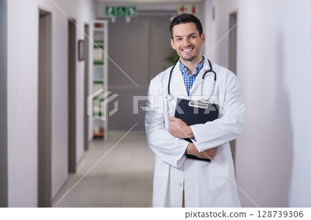Asian male doctor standing in hospital corridor holding clipboard with stethoscope, copy space Asian male doctor standing in hospital corridor holding clipboard with stethoscope, copy space 128739306