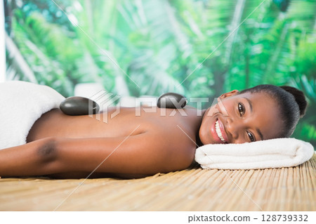 Young African American woman receiving hot stone massage on bamboo mat in spa, with black stones Young African American woman receiving hot stone massage on bamboo mat in spa, with black stones 128739332