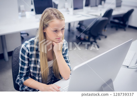 Teenage girl sitting at white desk in computer lab using all-in-one computer and mouse, copy space 128739337