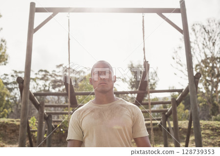 Man standing at outdoor obstacle course clearing, featuring hanging ropes and wooden boards 128739353