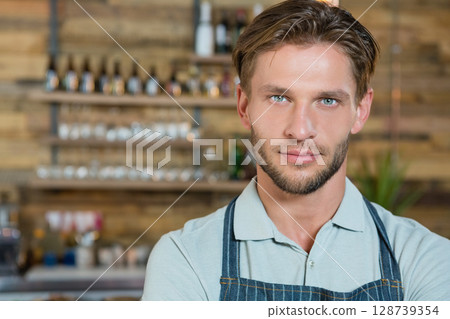 Young man serving drinks in rustic wooden bar, featuring liquor bottles and glassware, copy space 128739354