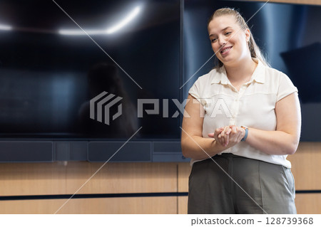 Smiling woman standing confidently in conference room, with wall-mounted monitors, copy space 128739368