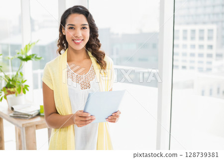 Holding tablet woman standing in office beside wooden table with plant and documents, copy space 128739381