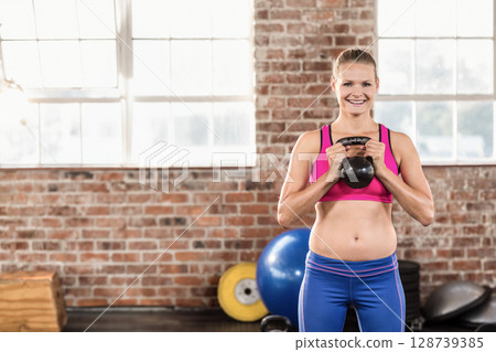 Woman lifting black kettlebell at chest in brick gym, with exercise ball, copy space Woman lifting black kettlebell at chest in brick gym, with exercise ball, copy space 128739385