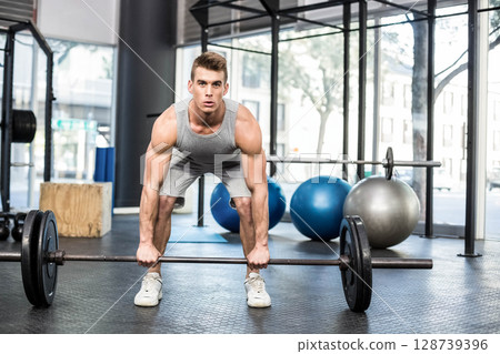 Lifting man performing deadlift on rubber mats at commercial gym, with barbell and stability balls 128739396