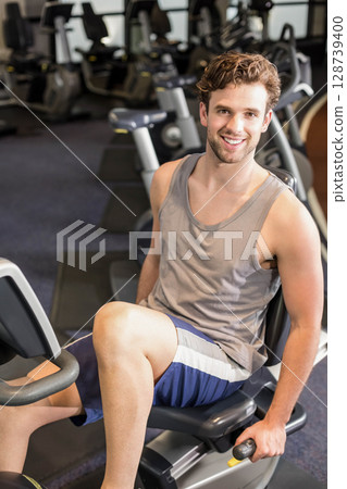 Pedaling man gripping handlebars on recumbent bike in gym, viewing digital display Pedaling man gripping handlebars on recumbent bike in gym, viewing digital display 128739400