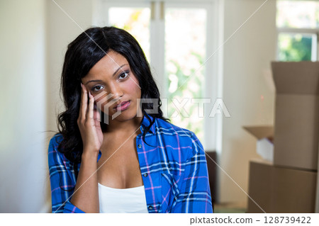 Resting head on hand, woman gazing at bright window in hallway, with stacked moving boxes 128739422