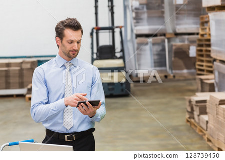Man operating tablet in warehouse storage area, with laptop on cart, forklift and pallets of boxes Man operating tablet in warehouse storage area, with laptop on cart, forklift and pallets of boxes 128739450