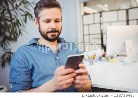 Scrolling mid adult man checking smartphone at office desk, with screen and coffee cup 128739483