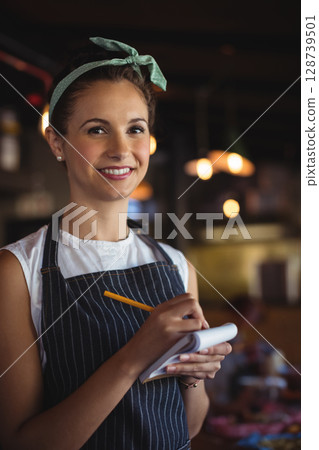 Smiling female server taking orders in cozy restaurant interior, with notepad and pencil 128739501