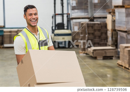 Holding boxes, man in safety vest standing in warehouse with forklift and pallets, copy space 128739506