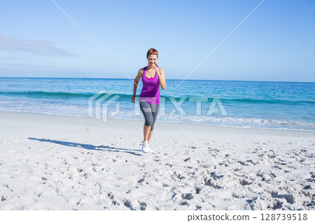 Woman jogging on white sandy beach at shoreline, wearing purple tank top and white running shoes 128739518