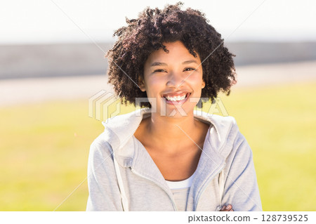 Smiling African American woman wearing grey hoodie standing in grassy park, with white shirt 128739525