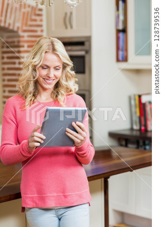Leaning woman holding tablet and browsing recipes at home kitchen counter, showing cookbooks 128739536