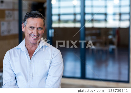 Smiling man standing in modern office, with glass partition and corkboard, copy space Smiling man standing in modern office, with glass partition and corkboard, copy space 128739541
