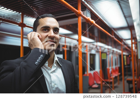 Talking man standing inside subway car, holding smartphone by ear near orange handrails, copy space Talking man standing inside subway car, holding smartphone by ear near orange handrails, copy space 128739548