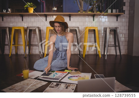 Reviewing female artist selecting sketches on wooden floor in studio, with tablet and orange juice Reviewing female artist selecting sketches on wooden floor in studio, with tablet and orange juice 128739555