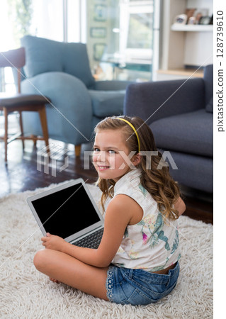 Sitting girl child using silver laptop on white shag rug in living room, with daylight streaming Sitting girl child using silver laptop on white shag rug in living room, with daylight streaming 128739610