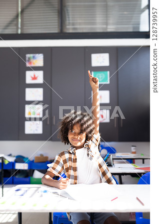 Diverse school-age boy arranging loose papers and pencils on desk in primary school classroom Diverse school-age boy arranging loose papers and pencils on desk in primary school classroom 128739957