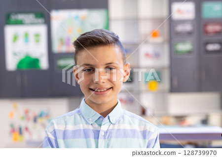 Teenage boy smiling at camera in art classroom, with colorful artwork and charts pinned on cabinets Teenage boy smiling at camera in art classroom, with colorful artwork and charts pinned on cabinets 128739970