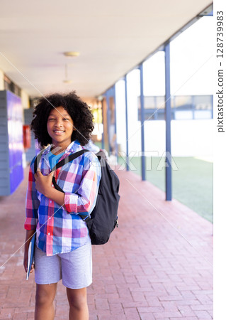 African American boy standing in walkway with purple lockers, holding notebook and backpack strap African American boy standing in walkway with purple lockers, holding notebook and backpack strap 128739983