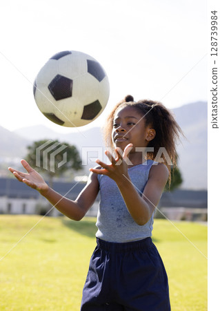 African American girl catching black-and-white soccer ball on grassy park field, showing skill 128739984