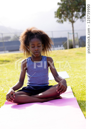 African American child practicing yoga on grassy lawn with pink mat, with second mat behind African American child practicing yoga on grassy lawn with pink mat, with second mat behind 128739990