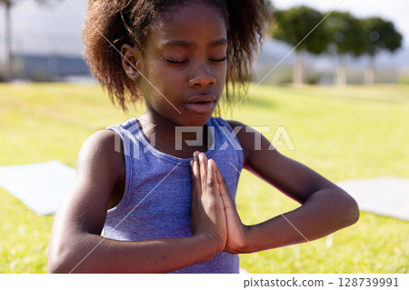 African American child girl meditating on yoga mat in public park, finding inner peace African American child girl meditating on yoga mat in public park, finding inner peace 128739991