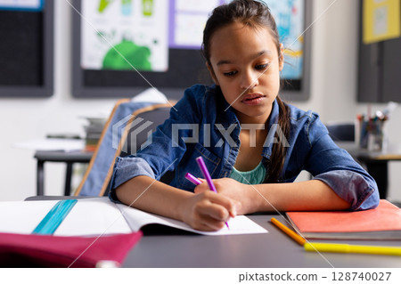 Child girl writing with purple pen in notebook at elementary classroom desk with binder, copy space Child girl writing with purple pen in notebook at elementary classroom desk with binder, copy space 128740027