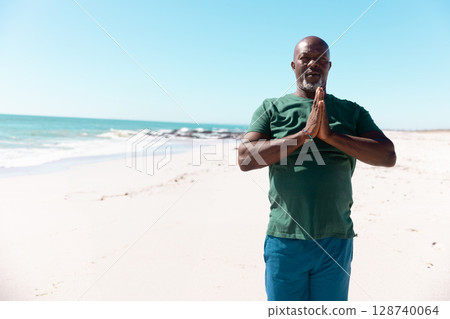 Senior African American man standing near shore on beach, pressing palms with bracelet, copy space Senior African American man standing near shore on beach, pressing palms with bracelet, copy space 128740064