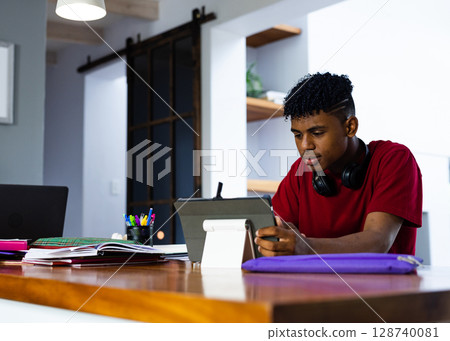 Teenage boy sitting at table in home study using tablet stand with notebooks, copy space Teenage boy sitting at table in home study using tablet stand with notebooks, copy space 128740081
